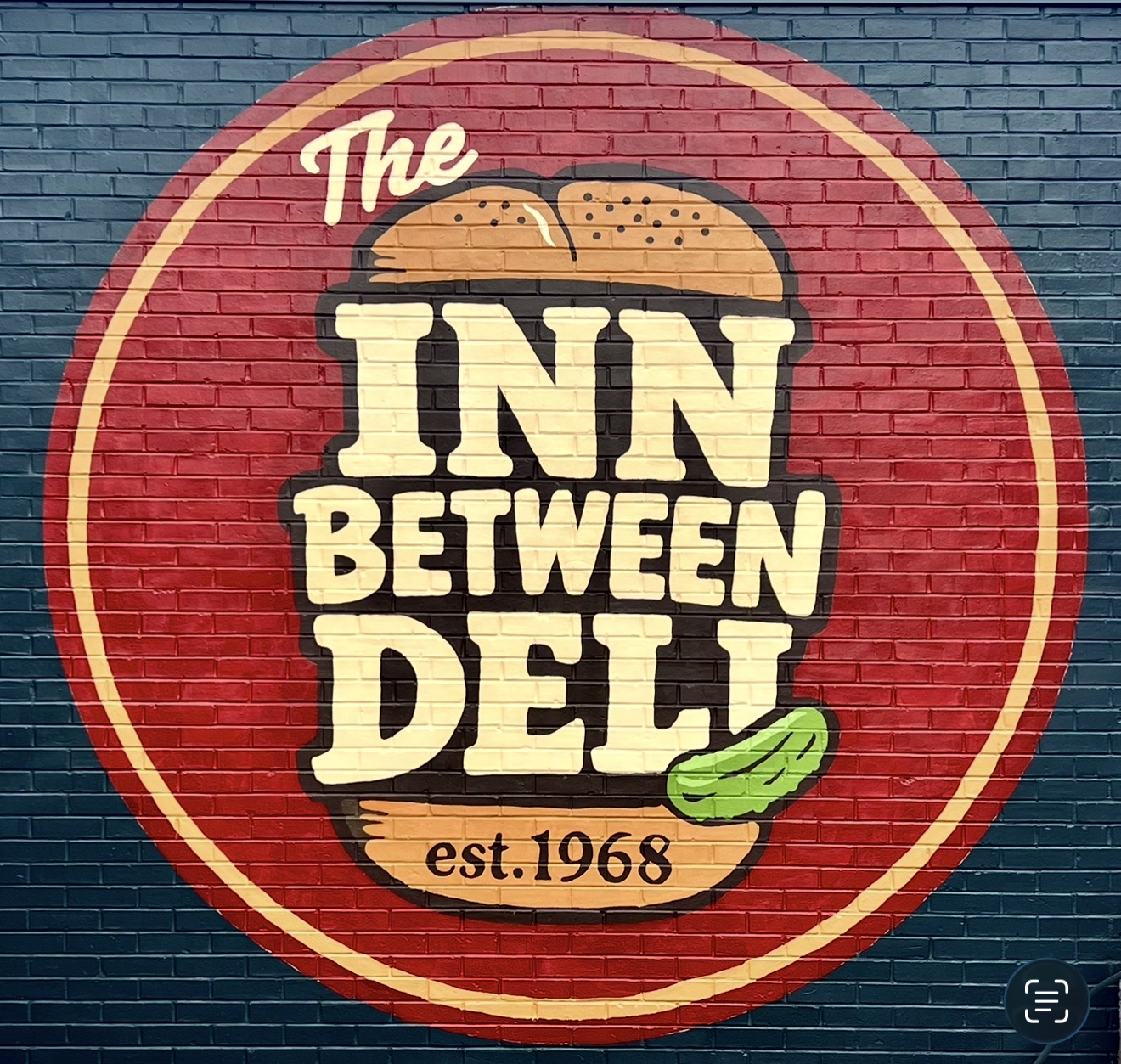The deli's round Inn-Between logo painted on the brick wall